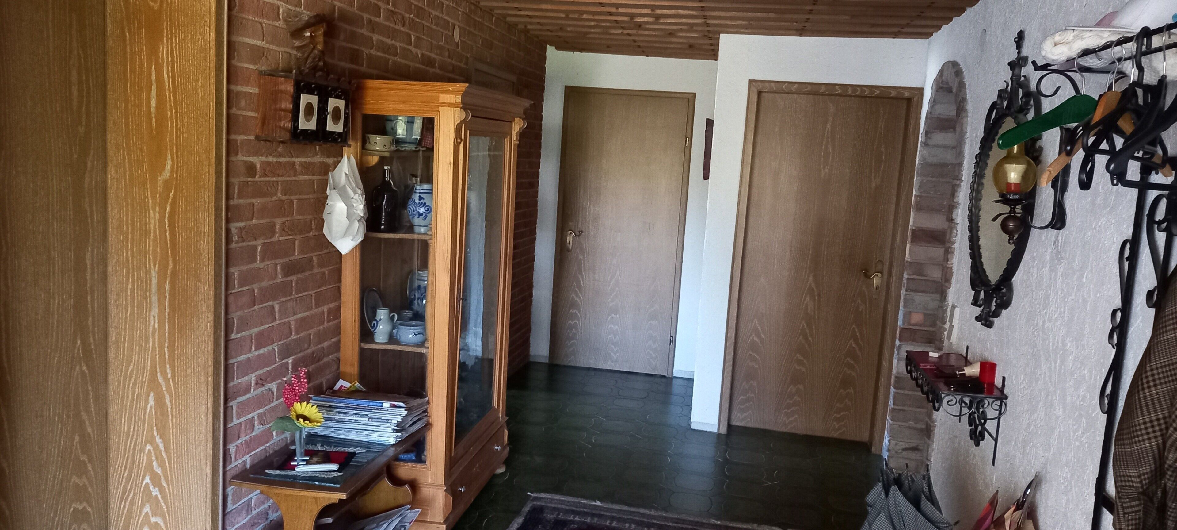A hallway with a wooden cabinet, a door, and a wall-mounted rack with hooks.