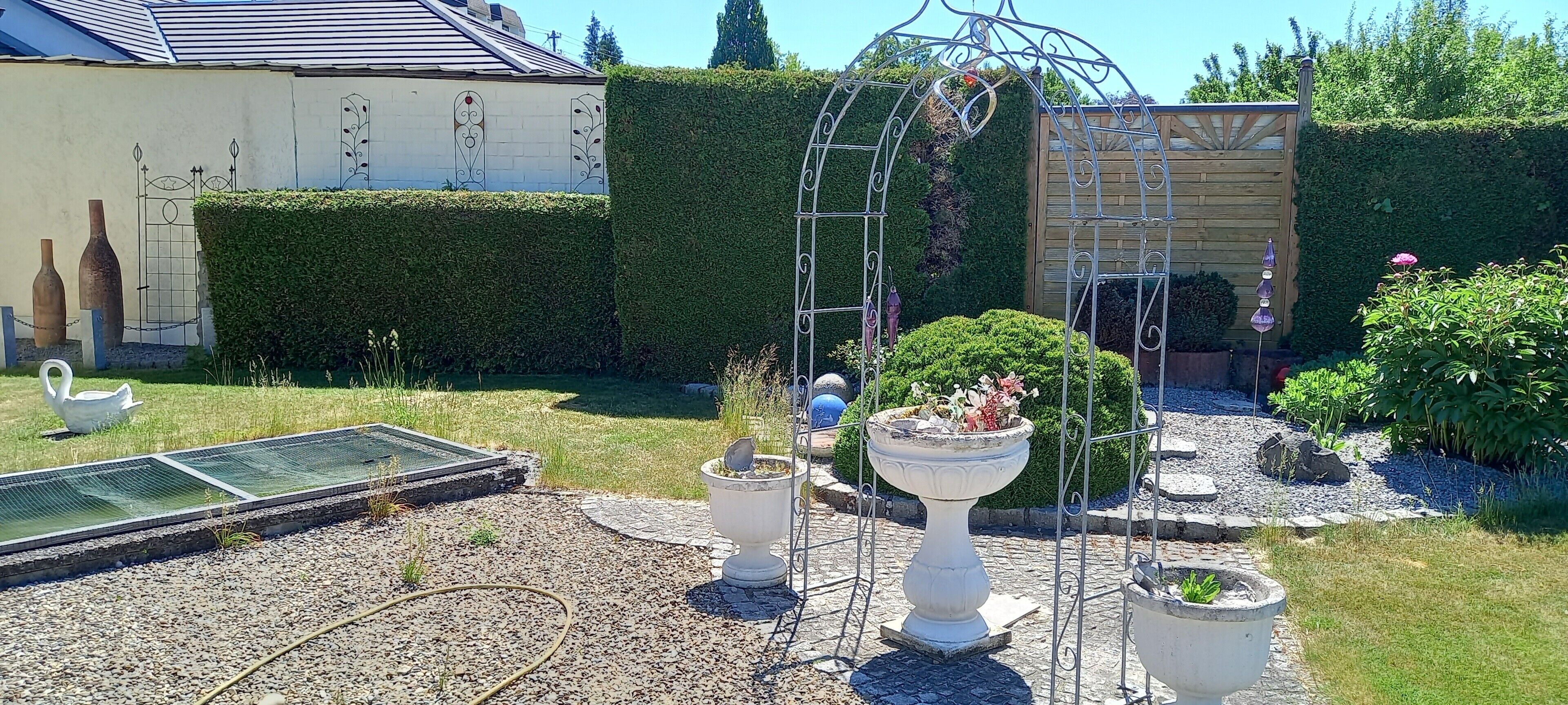 Un jardin agrémenté d’une tonnelle en métal, d’un abreuvoir pour oiseaux et d’une fontaine décorative.