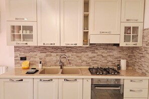 A kitchen with white cabinets, a double sink, a gas stove, and a tiled backsplash. - In the Como Borghi Area (Ganymede Apartment) (Como)