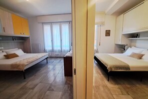 A hotel room with two beds, a wooden floor, a view through a door, and a window with curtains. - In the Como Borghi Area (Ganymede Apartment) (Como)