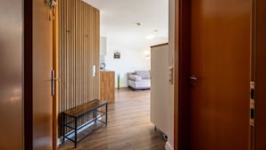 Ein Korridor mit einer Holzbank, einer Holzwand und einer Tür zu einem Wohnbereich mit Sofa und Couchtisch.