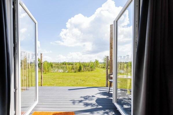 An open sliding glass door leading to a deck with a view of a grassy field and trees.