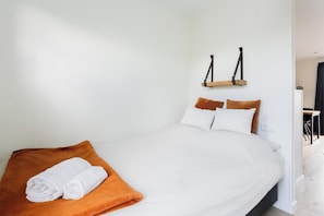 Una cama bien hecha con ropa de cama blanca y marrón, un edredón marrón y toallas blancas enrolladas.