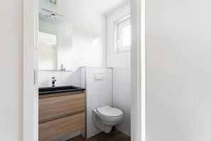 Um banheiro compacto com vaso sanitário branco, espelho e toucador de madeira.
