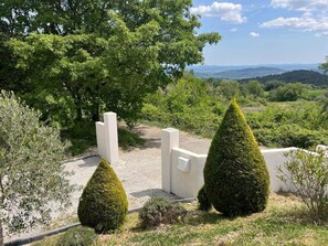 Un espace aménagé avec des haies taillées, un chemin de gravier et une structure murale blanche.