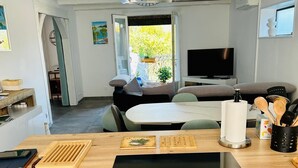 Una cocina compacta con estufa integrada, un comedor con mesa y sillas, y un televisor al fondo.