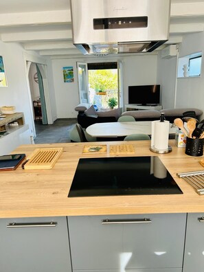 A compact kitchen with a built-in stove, a dining area with a table and chairs, and a TV in the background. - Renovated family home with sea view, swimming pool and terrace, 10min walk from the beach (Carqueiranne)