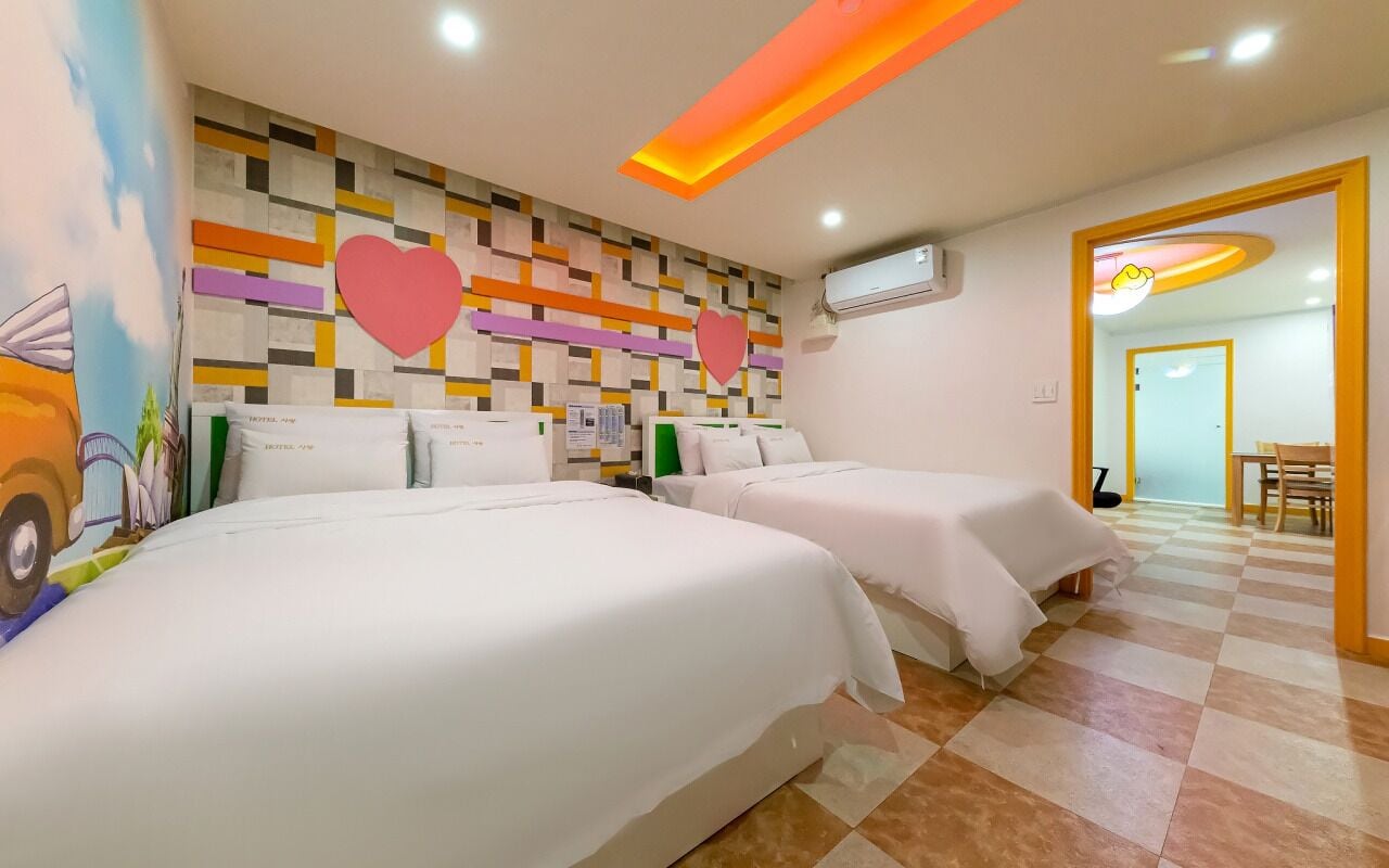 A hotel room with two beds, a checkered floor, a wall with a geometric pattern, and a ceiling with a linear light fixture.