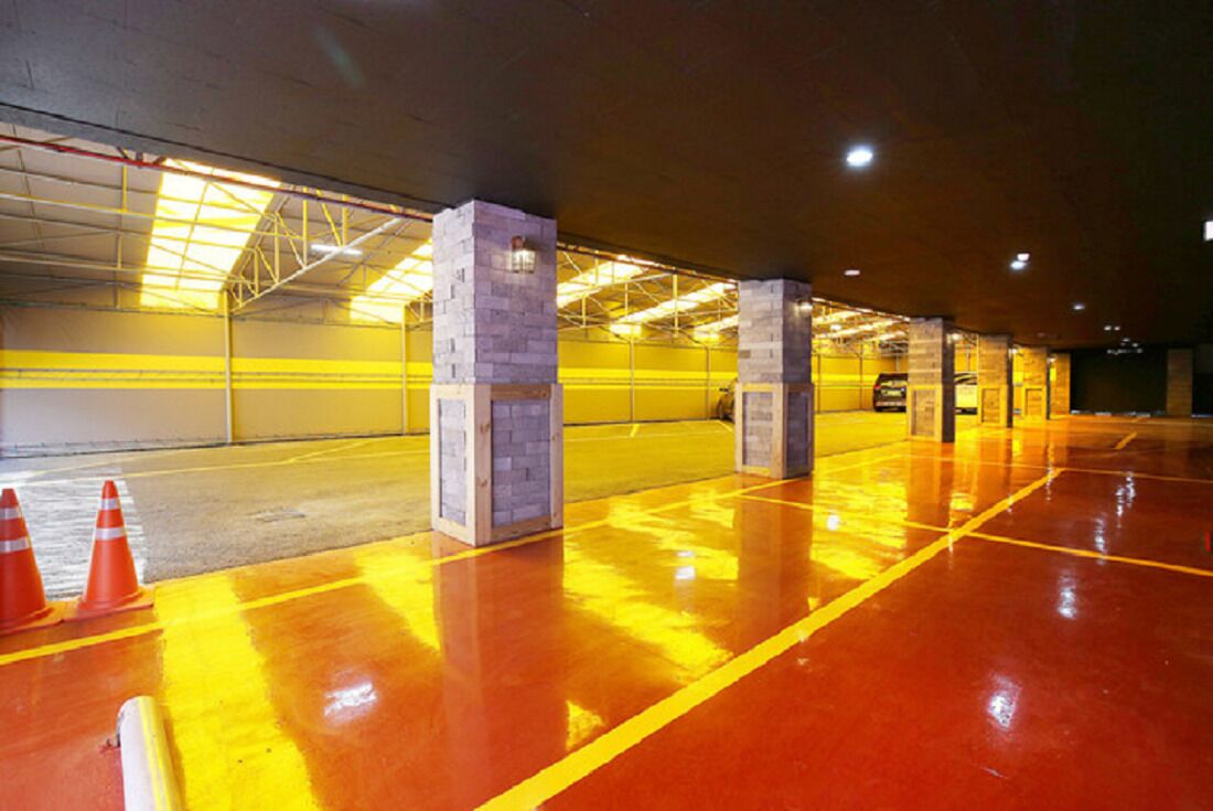 Een parkeergarage met gele lijnen, betonnen pilaren en oranje verkeerspalen.
