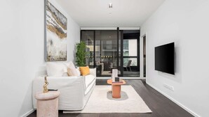 A modern living room with a white sofa, a coffee table, a TV, and a large window. - LaneStay - Premium 2BR Retreat, Parking & Pool & Gym (Melbourne)