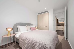 Una camera da letto con un letto, lampade sui comodini, un armadio e un bagno parzialmente visibile attraverso una porta aperta.