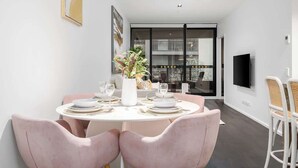 A modern dining area with a round table, pink chairs, and a vase of flowers. - LaneStay - Premium 2BR Retreat, Parking & Pool & Gym (Melbourne)
