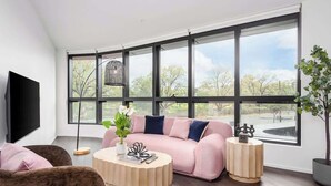 A modern living room with a large window, a sofa, a coffee table, and a TV. - LaneStay - 2BR Albert Park Views, Pool Gym Parking (Melbourne)