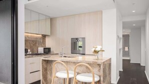 A modern kitchen with a marble island, two bar stools, a refrigerator, and a microwave. - LaneStay - 2BR Albert Park Views, Pool Gym Parking (Melbourne)