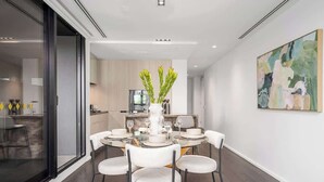 A modern dining room with a glass partition, a central white vase with greenery, and a contemporary abstract painting on the wall. - LaneStay - Albert Park Views with Pool Gym Parking (Melbourne)