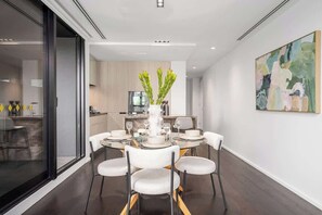 A modern dining room with a glass partition, a central white vase with greenery, and a contemporary abstract painting on the wall. - LaneStay - Albert Park Views with Pool Gym Parking (Melbourne)