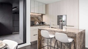 A modern kitchen with a marble island, white bar stools, and a built-in oven. - LaneStay - Albert Park Views with Pool Gym Parking (Melbourne)
