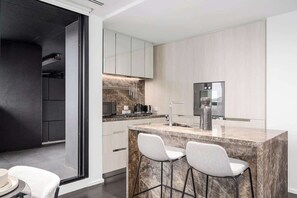 A modern kitchen with a marble island, white bar stools, and a built-in oven. - LaneStay - Albert Park Views with Pool Gym Parking (Melbourne)