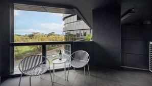 A modern balcony with two chairs and a table, large windows offering a view of a road and greenery. - LaneStay - Albert Park Views with Pool Gym Parking (Melbourne)