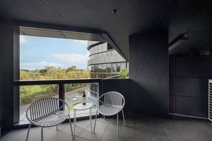 A modern balcony with two chairs and a table, large windows offering a view of a road and greenery. - LaneStay - Albert Park Views with Pool Gym Parking (Melbourne)