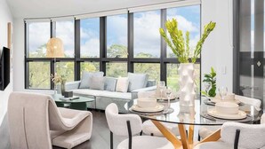 A modern interior with a dining area, a sofa, and large windows. - LaneStay - Albert Park Views with Pool Gym Parking (Melbourne)