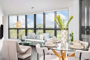 A modern interior with a dining area, a sofa, and large windows. - LaneStay - Albert Park Views with Pool Gym Parking (Melbourne)