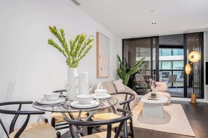 A modern living room with a glass dining table, black chairs, a sofa, and a coffee table. - LaneStay - Lakeside Luxury with Pool, Gym, Parking (Melbourne)