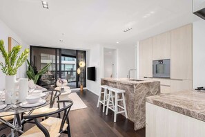 A modern kitchen with a marble countertop, a built-in oven, and a flat-screen TV. - LaneStay - Lakeside Luxury with Pool, Gym, Parking (Melbourne)
