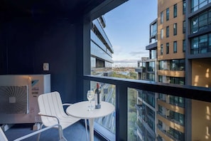 A balcony with a white chair, a small table, and a bottle of wine. - LaneStay - Lakeside Luxury with Pool, Gym, Parking (Melbourne)