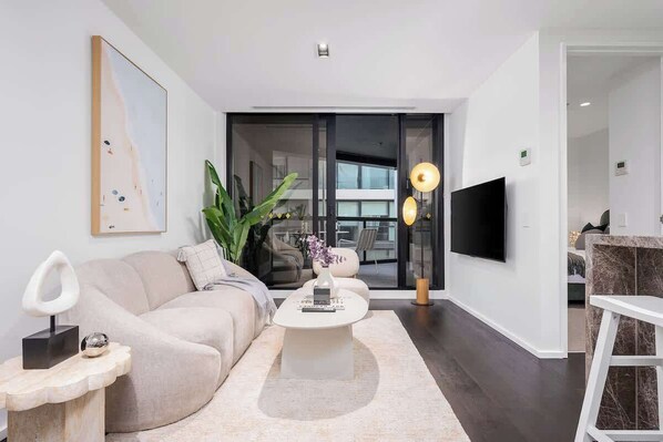 A modern living room with a sofa, coffee table, and a TV mounted on the wall. - LaneStay - Lakeside Luxury with Pool, Gym, Parking (Melbourne)