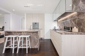 A modern kitchen with a marble island, white stools, and a built-in oven. - LaneStay - Lakeside Luxury with Pool, Gym, Parking (Melbourne)