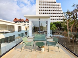 Ein moderner Balkon mit Glasgeländern, einer Sitzecke mit Stühlen und einem Tisch sowie Blick auf einen Hochhaus im Hintergrund.