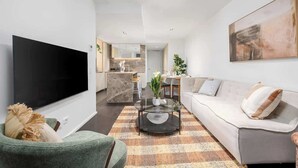 A modern living room with a flat-screen TV, a sofa, a coffee table, and a kitchen in the background. - LaneStay - Luxury Living with Pool, Gym & Parking (Melbourne)