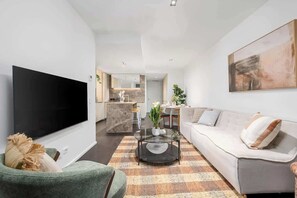 A modern living room with a flat-screen TV, a sofa, a coffee table, and a kitchen in the background. - LaneStay - Luxury Living with Pool, Gym & Parking (Melbourne)