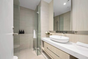 A modern bathroom with a glass shower enclosure, a white sink, and a large mirror. - LaneStay - Luxury Living with Pool, Gym & Parking (Melbourne)