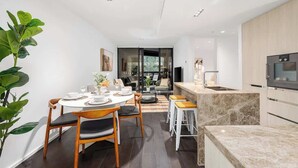 A modern kitchen with a built-in oven, a dining area with a round table and chairs, and a large plant. - LaneStay - Luxury Living with Pool, Gym & Parking (Melbourne)