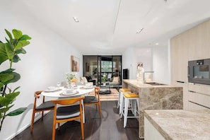 A modern kitchen with a built-in oven, a dining area with a round table and chairs, and a large plant. - LaneStay - Luxury Living with Pool, Gym & Parking (Melbourne)