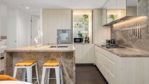 A modern kitchen with a central island, white bar stools, and a built-in microwave. - LaneStay - Luxury Living with Pool, Gym & Parking (Melbourne)