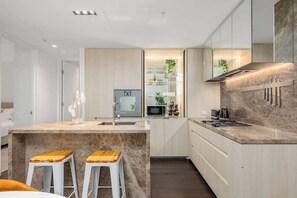 A modern kitchen with a central island, white bar stools, and a built-in microwave. - LaneStay - Luxury Living with Pool, Gym & Parking (Melbourne)