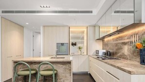 Een moderne keuken met een marmeren aanrechtblad, ingebouwde apparatuur en een centraal eiland met barstoelen.