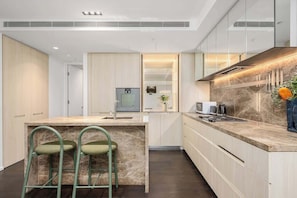 A modern kitchen with a marble countertop, built-in appliances, and a central island with bar stools. - LaneStay - Lakeside Luxury w Pool, Gym & Parking (Melbourne)