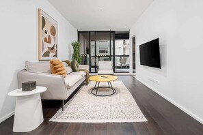 A modern living room with a sofa, a coffee table, a TV, and a large window. - LaneStay - Lakeside Luxury w Pool, Gym & Parking (Melbourne)