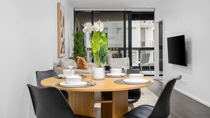 Een moderne eetruimte met een ronde tafel, zwarte stoelen, wit servies en een potplant.
