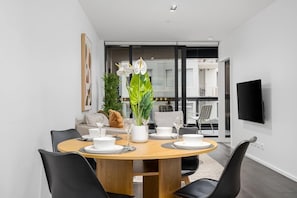 A modern dining area with a round table, black chairs, white tableware, and a potted plant. - LaneStay - Lakeside Luxury w Pool, Gym & Parking (Melbourne)