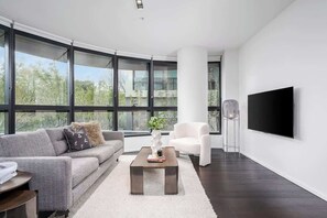 Ein modernes Wohnzimmer mit Sofa, Sesseln, Couchtisch und einem an der Wand montierten Flachbildfernseher.