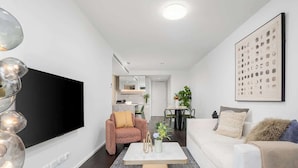 Ett modernt vardagsrum med en platt-TV, en soffa, ett soffbord och en matplats i bakgrunden.