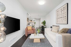 A modern living room with a flat-screen TV, a sofa, a coffee table, and a dining area in the background. - LaneStay - Albert Park View w Pool, Gym & Parking (Melbourne)