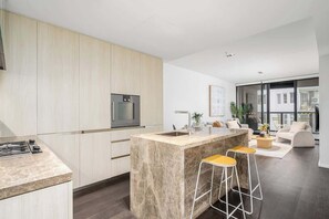 A modern kitchen with a marble island, stainless steel appliances, and a bar area with stools. - LaneStay - Elevated 2B2B w Pool, Gym and Parking (Melbourne)