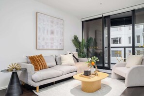 A modern living room with a sofa, coffee table, and a large window. - LaneStay - Elevated 2B2B w Pool, Gym and Parking (Melbourne)