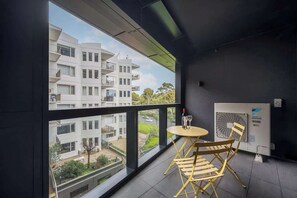 A balcony with a view of a modern building, a table with chairs, and an air conditioning unit. - LaneStay - Elevated 2B2B w Pool, Gym and Parking (Melbourne)